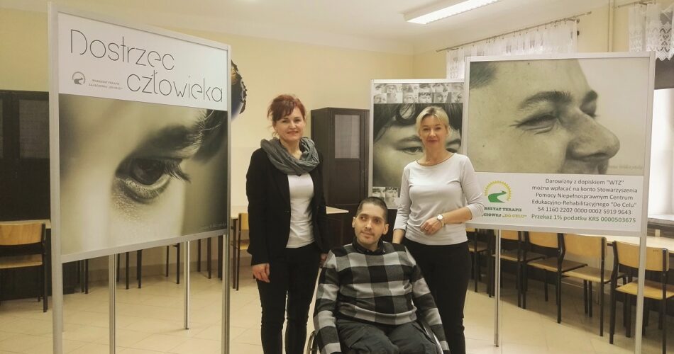 Zdjęcie przedstawia autora oraz dwie panie pracujące w Stowarzyszeniu Nowe Perspektywy w Radomiu. W tle znajduje się wystawa zdjęć osób z niepełnosprawnościami zatytułowana "Dostrzec człowieka".